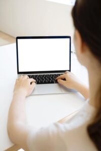 Woman is typing in a laptop with a blank screen