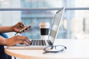 Person working in a laptop while holding a mobile phone